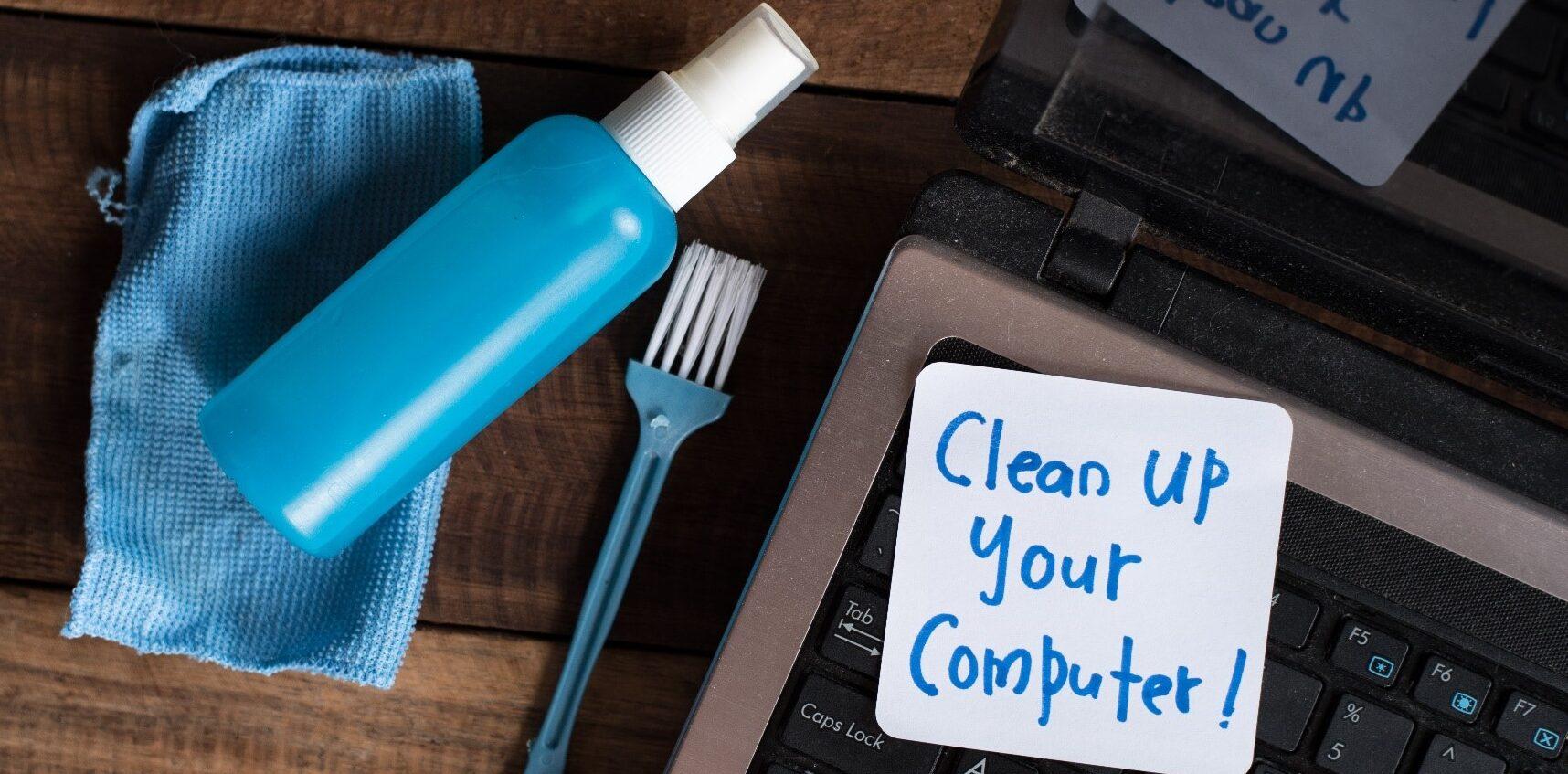A computer keyboard with a note on it saying 'Clean up your computer!' along with a screen cleaning spray and cloth.