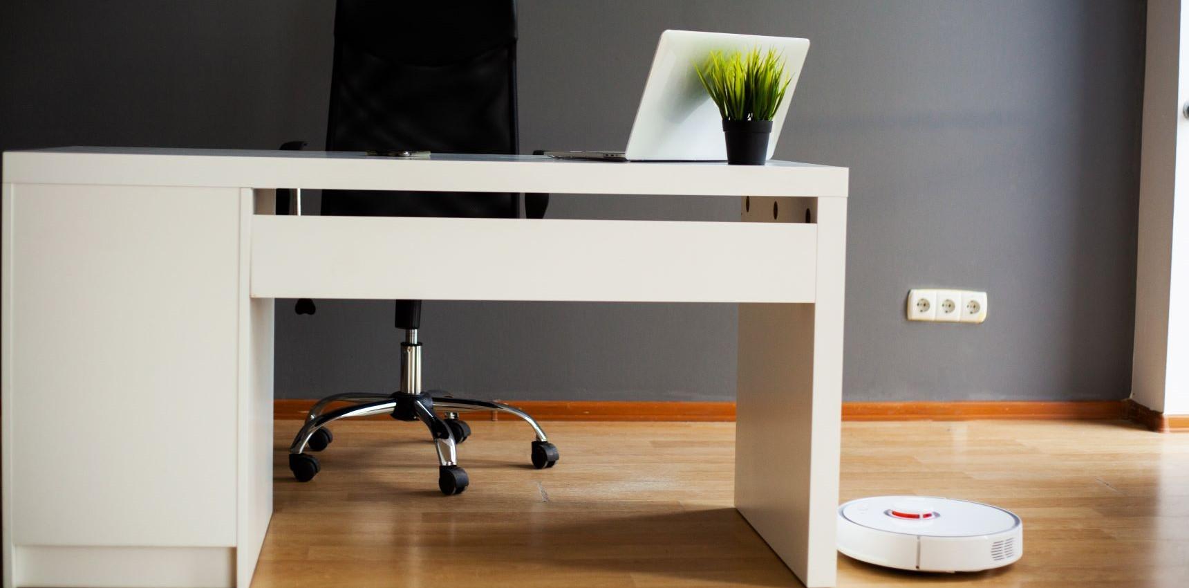 An office desk and chair, laptop and robot vacuum cleaner