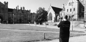 Photographer Nate Landsell, stands in front of a large building taking a shot of it.